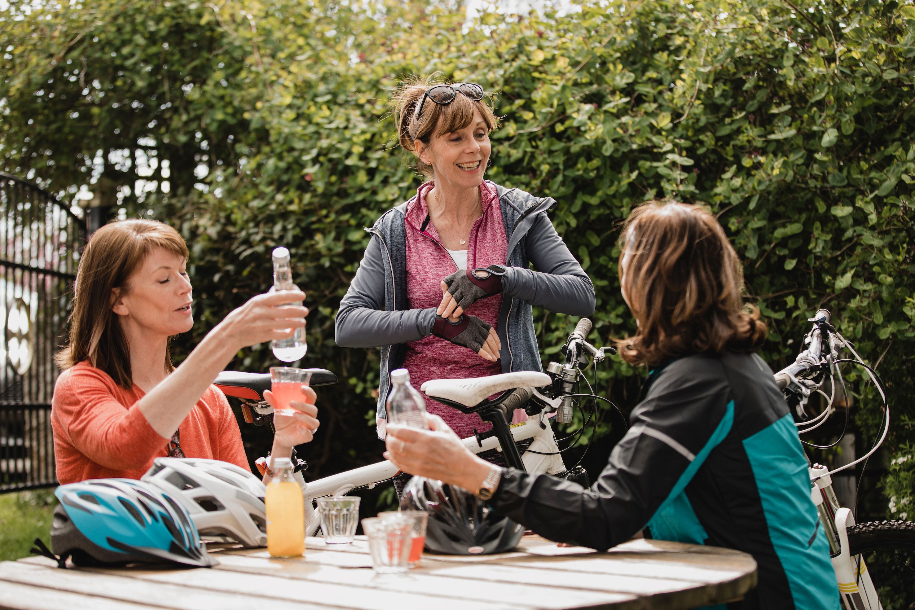 three middle-aged female cyclists chatting around an outdoor table